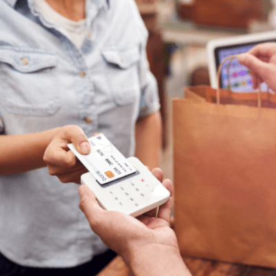 Close up of woman in store making contactless payment at sales desk holding credit card to reader